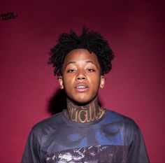 a young man with tattoos on his neck standing in front of a red wall