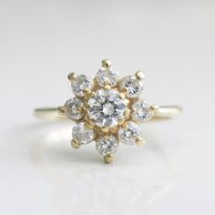 a yellow gold and white diamond ring on a white surface with the center stone surrounded by smaller diamonds