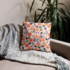 an orange print pillow sitting on top of a couch next to a potted plant