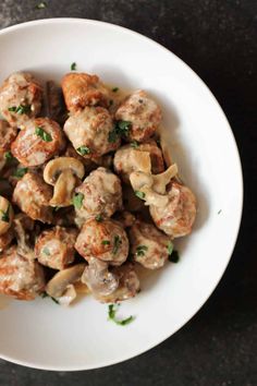 a white bowl filled with meatballs covered in sauce and parsley on the side