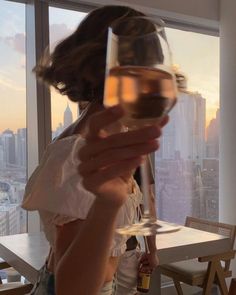 a woman holding up a wine glass in front of a window with the city skyline outside