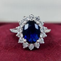 a blue and white diamond ring sitting on top of a red velvet box