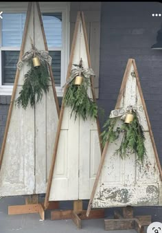 three wooden christmas trees sitting on the side of a building next to a door with greenery