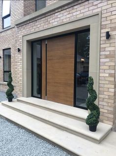 two potted plants sitting on the steps in front of a brick building with glass doors