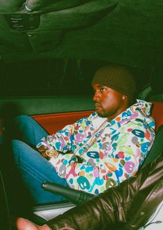 a man sitting in the back seat of a car wearing a colorful jacket and beanie