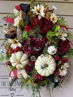 a wreath with white pumpkins, red flowers and leopard print ribbon hanging on the front door