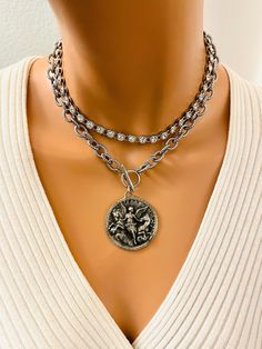 This is a super cool thick chain choker with pendant hanging from front toggle along with a rhinestone choker to add sparkle.  This very large pendant features a beautiful angel with horses, measures 40MM diameter and is made out of pewter. Chain is steel, links measure 11X8MM. Model is wearing a 16 inch length. Rhinestone choker above has spring clasp in back made of brass. This necklace is a set, you'll receive the choker and the pendant necklace. Available an antique silver or antique gold. T Silver Coin Pendant Choker, Catholic Jewelry Necklace, Jewelry Oxidized, Angel Pendant Necklace, Angel Necklace, Catholic Jewelry, Angel Pendant, Beautiful Angel, Rhinestone Choker