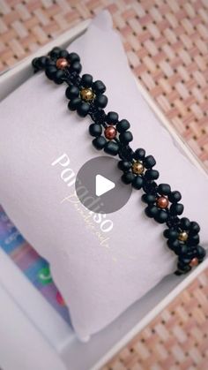 the beaded bracelet is in a white box with black beads and gold accents on it