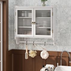 a white cabinet hanging from the side of a wall next to a sink and window