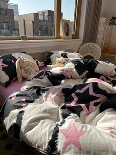 an unmade bed with pink and black stars on the comforter next to a window