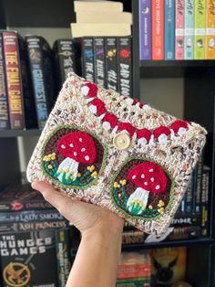 someone is holding up a crocheted wallet in front of some bookshelves