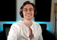 a man wearing headphones and sitting in front of a computer monitor smiling at the camera