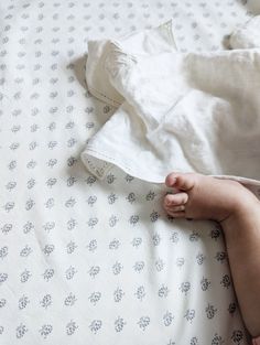 a baby's feet are laying on a bed with white sheets and blue flowers