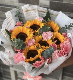 a bouquet of sunflowers and pink carnations in a paper wrapper