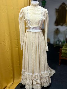 a white dress on display in front of a yellow curtain with a mannequin behind it