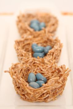 three birds nests with blue eggs in them on a white plate and one is made out of straw