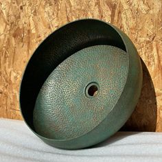 a green bowl sitting on top of a wooden table next to a white cloth covered wall