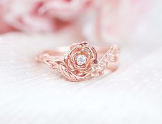 a rose shaped diamond ring sitting on top of a white blanket with pink flowers in the background