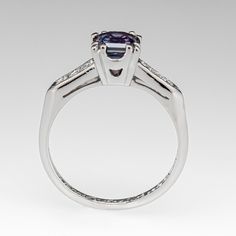 This gorgeous blue to purple color change sapphire engagement ring features a 1.16 carat no heat sapphire with Montana, USA origin that we sourced and set in a vintage platinum diamond mounting. The shoulders of the ring are each accented with three (3), channel set, round single cut diamonds, bordered with milgrain edging. The ring measures 6.2mm at the top, rises 6.3mm above the finger, tapering to 1.5mm wide and 1.3mm thick at the base of the shank. The ring is currently a size 5.75 and we offer complimentary resizing to fit. Classic Sapphire Rings In Purple, Classic Purple Sapphire Ring With Prong Setting, Classic Purple Sapphire Promise Ring, Purple Sapphire Ring With Brilliant Cut, Purple Sapphire Ring With Center Stone In Round Cut, Purple Sapphire Ring With Center Stone, Round Cut, Purple Tanzanite Ring With Brilliant Cut, Purple Sapphire Ring With Brilliant Cut For Anniversary, Purple Sapphire Ring With Round Cut And Prong Setting