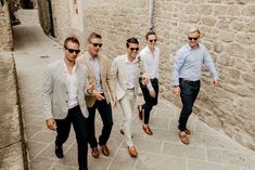 a group of men walking down a street next to a stone wall with sunglasses on