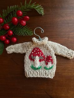 a knitted sweater ornament with red mushrooms on it next to holly branches