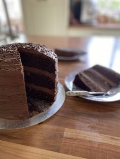 a chocolate cake sitting on top of a wooden table next to a slice of cake