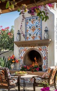 an outdoor fireplace and seating area with flowers on the table, potted plants around it