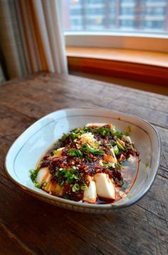 a white plate topped with food on top of a wooden table next to a window