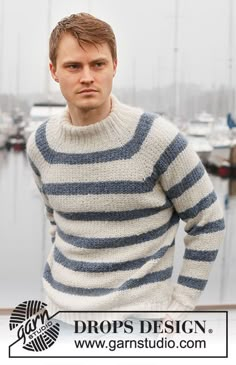 a man standing in front of a body of water wearing a blue and white striped sweater