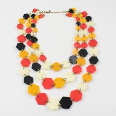 This sophisticated French artisan designer 1970s multi-strand necklace features three graduated rows of lucite geometric elements in a flat hexagonal shape. Typical assorted colors of the hippie period: black, neon orange, yellow marigold, and cream-white. There is no visible maker's mark. Measurements: The necklace's total length is 20.07 in (51 cm) - The largest element is 1.19 in wide (3 cm) x 1.07 in high (2.7 cm) - The font width is 7.50 in (19 cm).  Please see the measurements noted above Yellow Marigold, Geometric Elements, Black Neon, Maker's Mark, Multi Strand Necklace, Neon Orange, Strand Necklace, Multi Strand, Orange Yellow