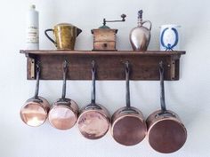 pots and pans are hanging on the wall above an old wooden shelf with hooks