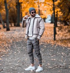 a man standing in the middle of a leaf covered park wearing a hat and jacket