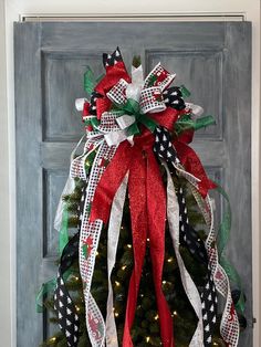 a christmas tree with red, white and green ribbons hanging on the front door for decoration