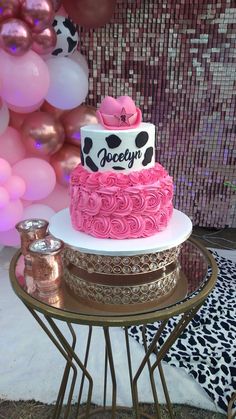 a pink and white cake sitting on top of a table next to some foil balloons