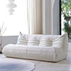 a white couch sitting in front of a window next to a vase on the floor