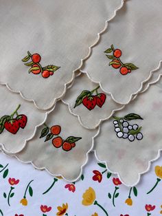 four embroidered napkins with cherries and berries on them are laying next to each other