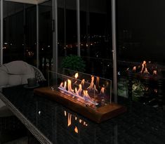 a glass fire pit sitting on top of a black counter next to a couch and window