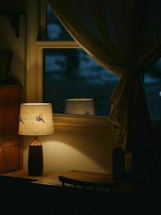 a lamp sitting on top of a wooden table next to a window in a dark room