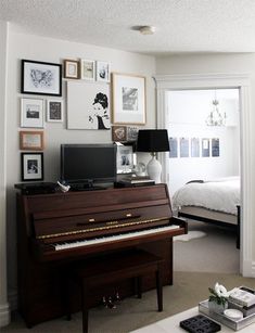 a living room with a piano and pictures on the wall next to a bed in it