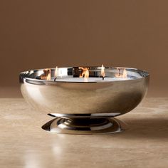 a silver bowl sitting on top of a table next to a brown wall with candles in it