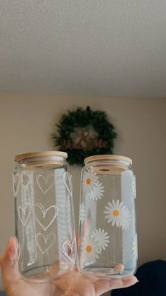 two mason jars with daisies painted on them are held in front of the camera