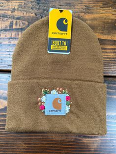 a brown beanie with a patch on the front and side of it, sitting on top of a wooden table