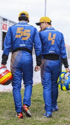 two men in blue racing suits holding helmets