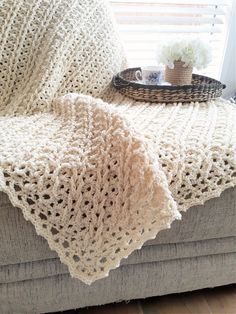 a white crocheted blanket sitting on top of a couch next to a basket