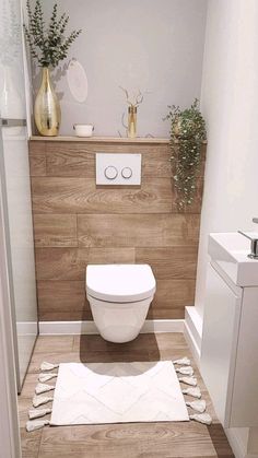 a white toilet sitting inside of a bathroom next to a wooden paneled wall with potted plants