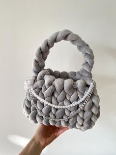 a hand holding up a basket made out of gray rocks with chains on the handle