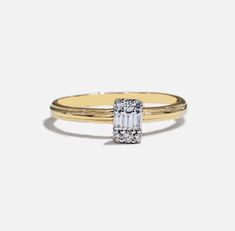 a yellow gold ring with an emerald cut diamond in the center, on a white background