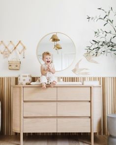 a baby sitting on top of a dresser next to a mirror