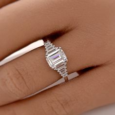 a woman's hand with a diamond ring on her left side and an emerald stone in the middle