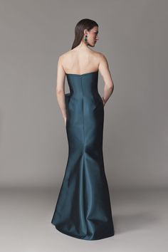 the back of a woman in a dark green gown, with her hands on her hips